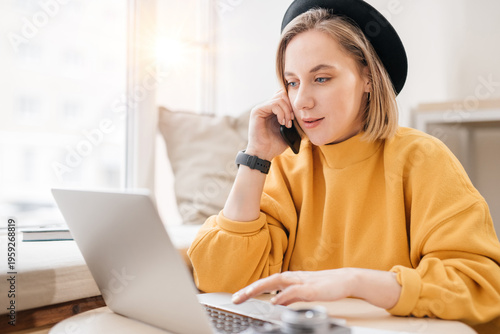 Woman using smart phone while working on laptop at cafe