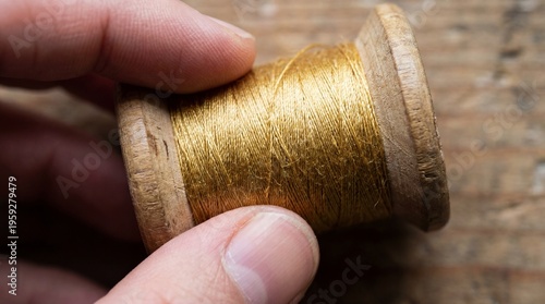 Top-Down Macro of Fingers Touching a Vintage Wooden Spool with Metallic Golden Thread