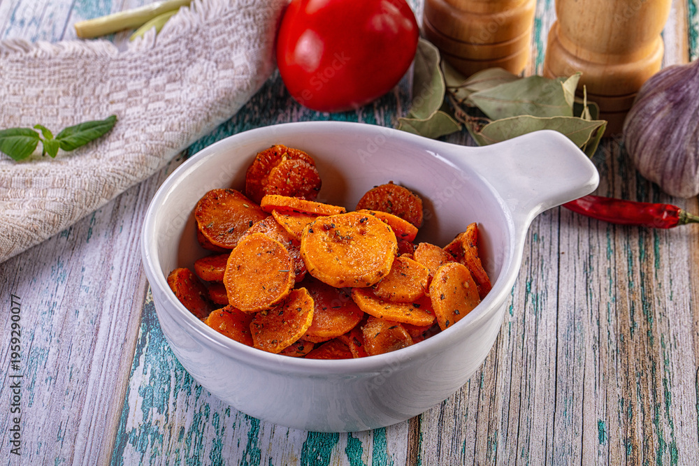 Fototapeta premium Roasted carrot slices with herbs in a white bowl on a rustic wooden background.