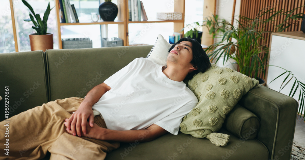 Obraz premium Thinking, sad and asian man relax on couch, introspection and self reflection for emotional processing. Rest, home and person with confirmation bias for experience memory, regret and remember mistake