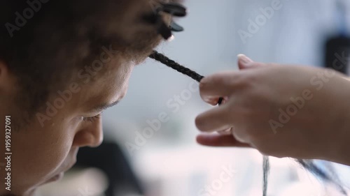 Close-up of professional hairdresser's hands braiding afro pigtails on a client's head. Detailed view of the hair styling process