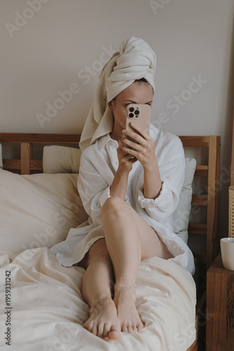 Young Woman Taking Selfie On Smartphone In Bed Wearing White Shirt and Hair Towel