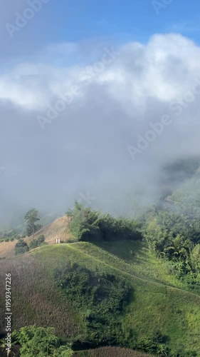 Panning shot of thick white mist and clouds flowing over lush green mountain peaks