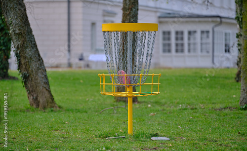 Discgolf basket with flying disc in front of mansion