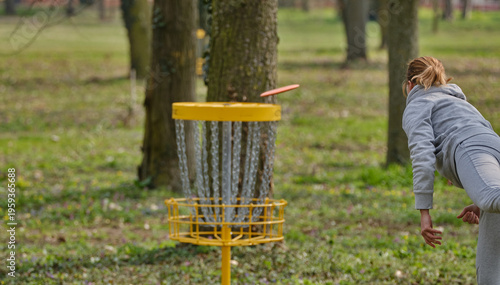 Discgolf basket with female player throwing a final shot