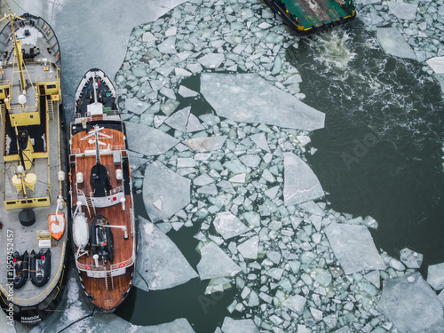 Aerial view of ships moored alongside the cold, ice-filled river, a study in contrasts between the rigid ice floes and the vessels' textured hulls, Gdansk, Poland.