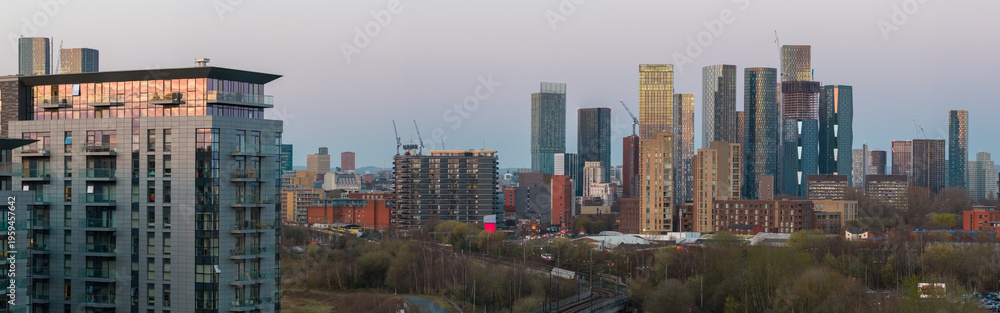 Fototapeta premium Aerial panorama featuring modern apartment blocks and the dense skyscraper cluster of Deansgate Square at dusk, Manchester, UK.
