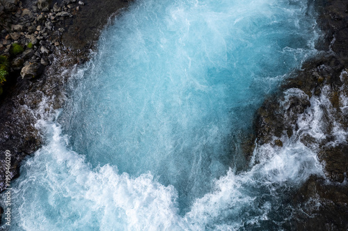 Stunning view of the Bruarfoss blue waterfall in Iceland, with turquoise water cascading over rocky terrain. Landscape of a tourist attraction and amazing travel destination.