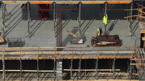 Drone shot capturing a construction worker handling formwork panels near reinforced concrete columns and scaffolding, highlighting structural preparation and active building process.
