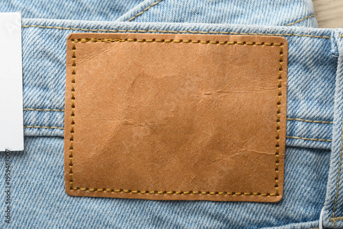 Blank brown leather label on light blue denim jeans with white paper tag, close up mockup for clothing brand identity design