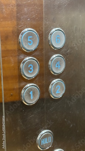Close-up shot of a scratched metal elevator control panel with blue backlit circular floor buttons.