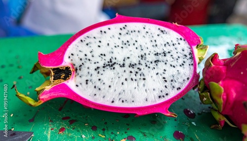 Close up of a halved white pitaya displaying seeds and vibrant pink peel at a market stall.