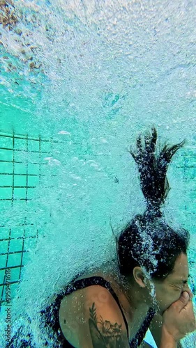 Tattooed woman in a swimsuit diving underwater into a pool