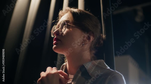 Close up of young adult female comedian with glasses shifting hands restlessly while revising speech standing backstage before live show