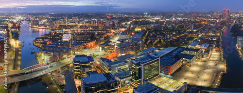 aerial panorama of the illuminated Salford Quays waterfront, the River Irwell, and the distant Manchester city skyline at night, UK.