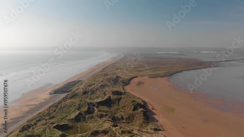 Drone camera glides smoothly over serene coastal landscape, revealing peaceful natural beauty and expansive open spaces for travel inspiration and wellness escapes.