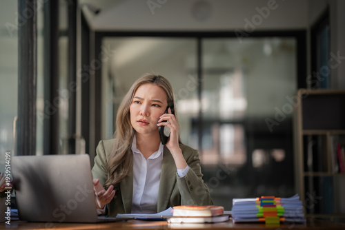 Foto Asian businesswoman talking on phone while working at office desk