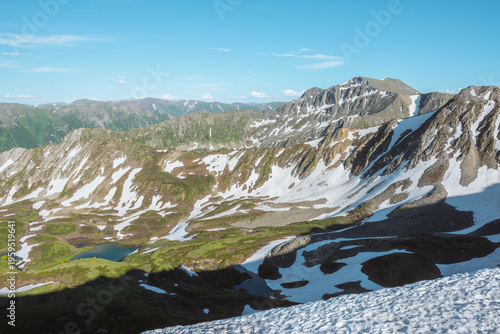Scenic view from snow-white glacier on precipice edge to alpine lake among sn...