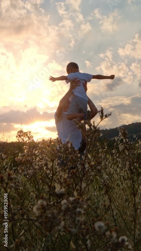 Weekend out of town with  family. Happy father lifting and spinning son in sunset field. An adult male raises his child into the golden sunset air in a wild meadow.