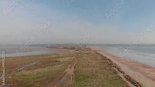 Drone glides over serene coastal landscape, revealing expansive sand dunes and gentle waves, inspiring freedom and natural beauty.