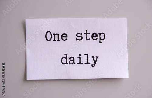 note saying 'one step daily' isolated on grey background, american typewriter font, motivation concept, power of small steps reminder