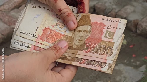 Pakistani Five Thousands  bank currency notes featuring multiple denominations held in hands with visible designs and colors