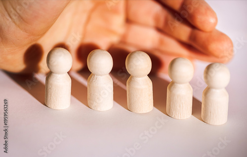 Hand positioned above five wooden figurines arranged in a row, showcasing different heights and shapes on a light surface, emphasizing craftsmanship and design