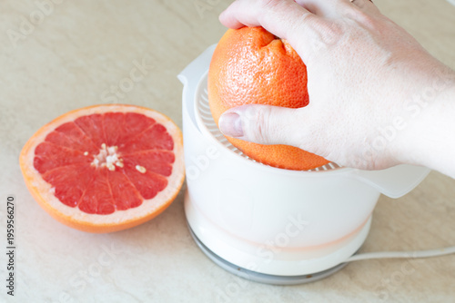 Hand pressing grapefruit on electric juicer preparing juice