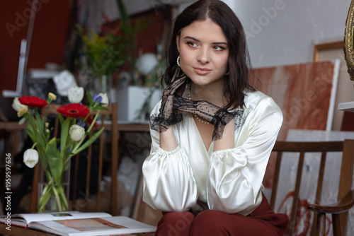 Artist elegant woman posing in an art studio, wearing a silk blouse, lace gloves, and pearls, reflecting creativity and style