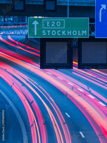 Road to Stockholm in Gothenburg Sweden shows busy traffic with motion lights at dusk leading to a green sign indicating direction