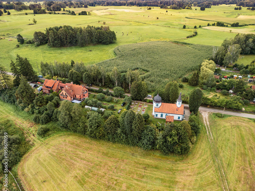 Drone view of Dormition of the Mother of God church, wooden bell tower, and small cemetery, Wojnowo