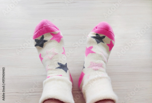 Person’s legs in colorful cotton socks on a light wooden background. Cozy home scene with crossed legs and a minimalist backdrop.