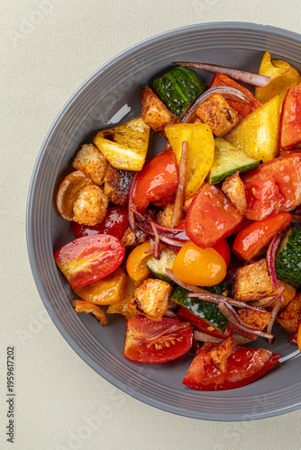 Warm roasted vegetables with tomatoes zucchini and crispy croutons served in gray bowl on light background
