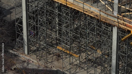 Drone view slowly panning over dense metal scaffolding surrounding a concrete building under construction, highlighting industrial framework, structure detail, and urban development progress.