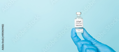Doctor hand in blue gloves holding DTaP vaccine vial over blue background. DTaP vaccine used to prevent diphtheria, tetanus, and pertussis.