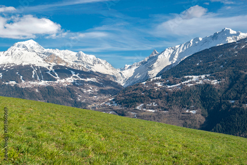 mountain landscape in spring with green meadows and snowy mountain peaks unde...