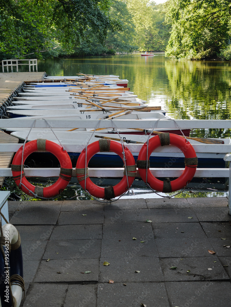 Fototapeta premium Orange Lifebuoy Ring and Rowboats Lined Up Along Wooden Dock Edge