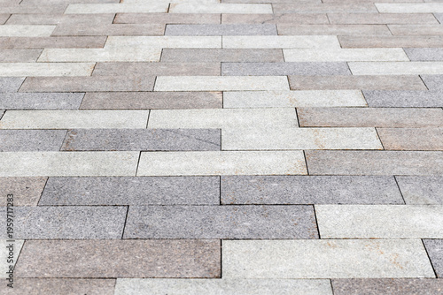 Fotografija A close-up view of textured stone paving on an urban walkway, featuring staggere