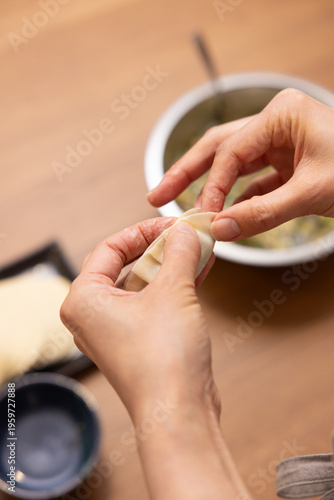 Close-up of hands wrapping gyoza filling in dumpling wrapper on wooden table