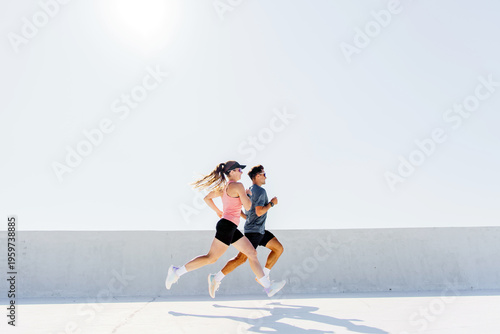 Athletic woman and man running actively together side-by-side during a bright outdoor fitness session