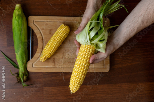 Photos Man's hands holding and shucking fresh corn on a wooden table