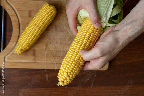 Tableau sur toile Male hands holding and shucking  fresh corn on the cob on a wooden table