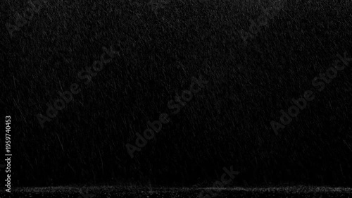 Wide shot of side windy rain with medium flow falling and landing on the ground with few bounces on a black background