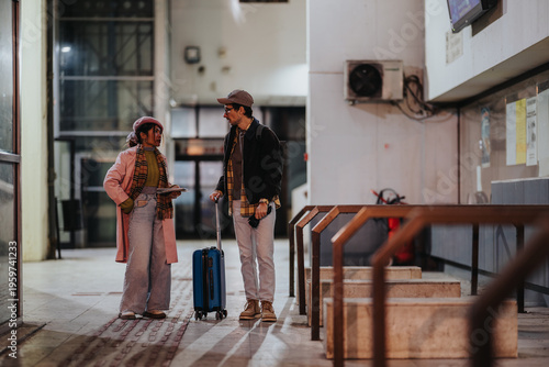 Foto A young couple of travelers talks while waiting in a transit station with a blue rolling suitcase