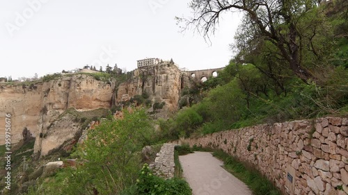 Stone paved trail along the El Tajo gorge leading to the famous Puente Nuevo bridge and historical architecture on high cliffs in Ronda, Andalusia.