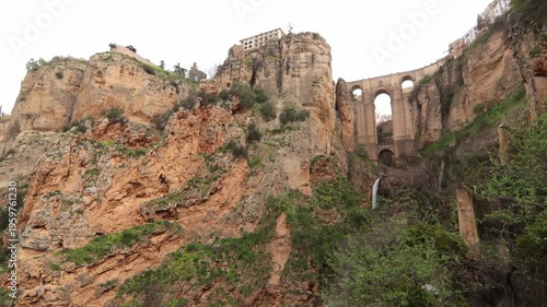 Dramatic low angle shot of the historic Puente Nuevo bridge spanning the deep Tajo gorge with a waterfall and rugged limestone cliffs in Ronda.