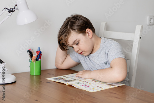 Young boy studying at home at wooden table. First grader with focused expression in cozy home study setting. Concepts of childhood learning, education and homework.