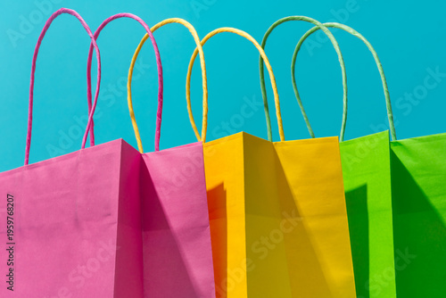 Close-up of colorful paper bags as summer sale and clearance sale concepts. Shopping paper bags on the turquoise blue background. Minimalist photo of pink, yellow and green bags.