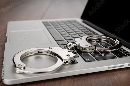 Closeup photo of handcuffs on modern laptop keyboard, symbolizing themes of restraint, cyber crime, justice and online security.
