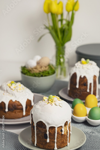 Traditional Easter cake Kulich with white glaze and yellow tulips on a festive table.